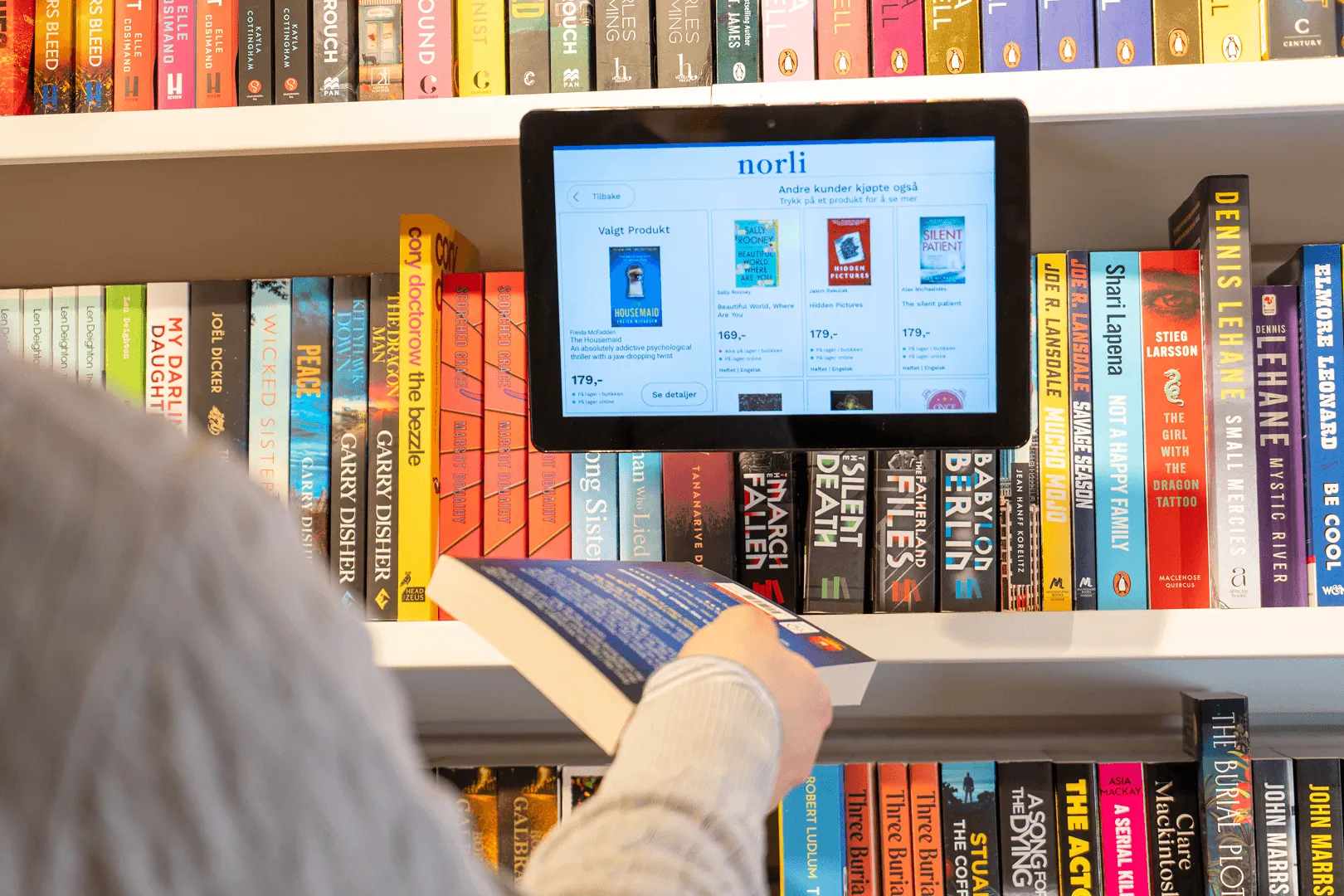 Customer scanning a book barcode on a Woopz price checker at Norli